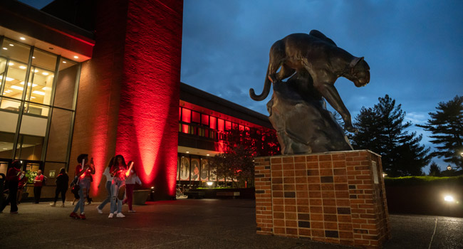 Three students of SIUE posing in various positions upon the 'e' located on campus