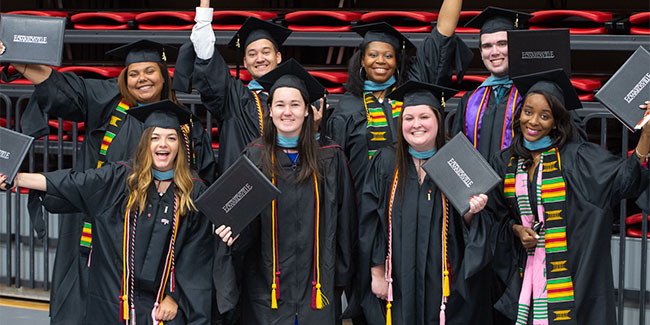 A group of graduates in their black cap and gown posing with their newly acquired degrees