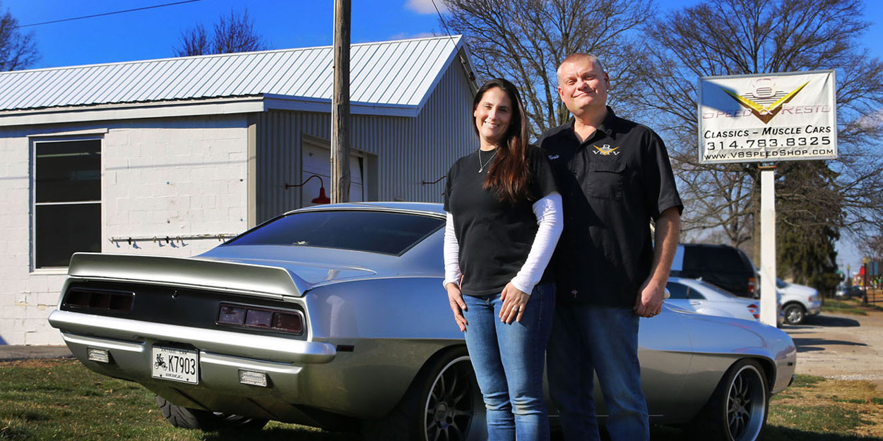 A man and a woman in front of car in front of a business.