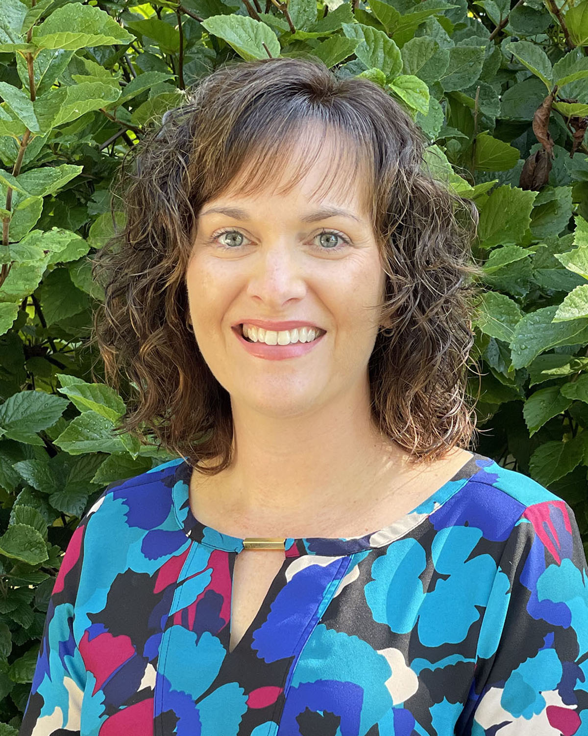 Jennifer Albat Headshot (outside with greenery in background)