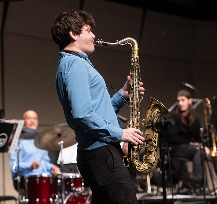 Cebulske playing the saxophone on stage at Katherine Dunham Theater. He appears to be wailing with his spine tilted back and his lungs filled with breath 