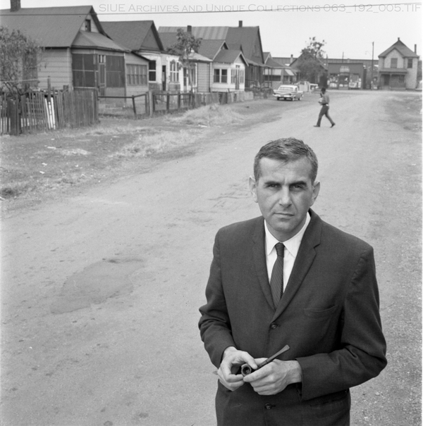 Rudwick standing in the foreground in the middle of a neighborhood street in East St Louis with a resident walking in the background