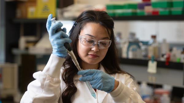 Student in goggles handles syringe in lab coat and lab