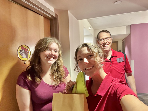 Three staffers in a selfie pose standing in front of resident hall inside doors