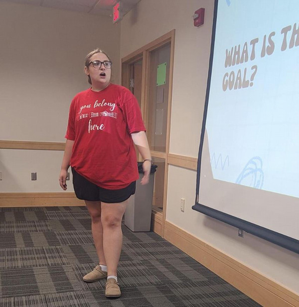 Woman in tshirt and shorts standing at projector screen talking about her presentation