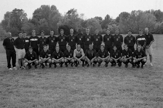 Black and white photo of the 2001 mens soccer team in grassy field with trees behind them