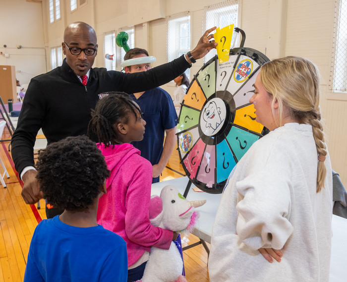 chancellor minor in the alton gym waiting area participating in a wheel spinning game with waiting dental patient kids