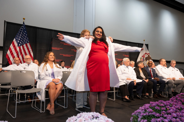 Student has white coat put on her by faculty member while on stage